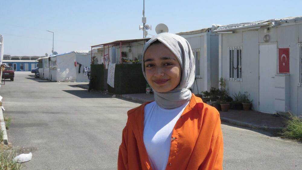 A girl wearing a scarf and an orange cloth is shown inside a container city.