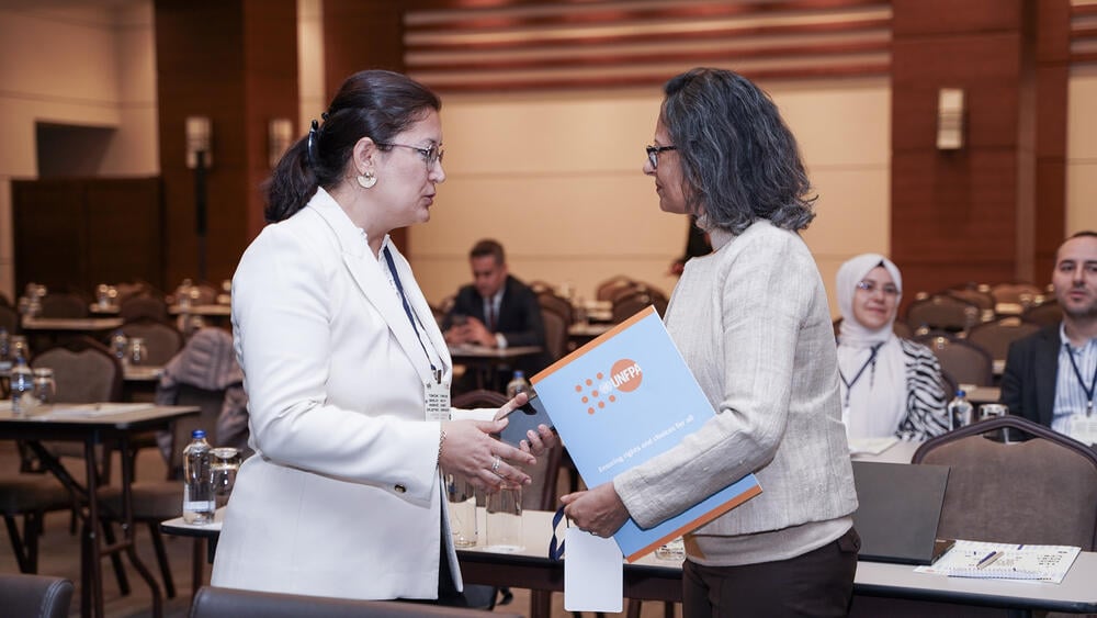 Two women, UNFPA Türkiye Representative Mariam Khan, on the right, shake hands in the event hall.