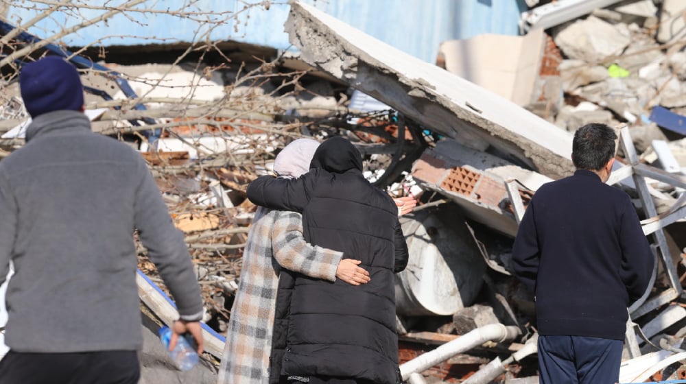 Depremzede iki kadın, çökmüş bir binanın önünde sarılıyor