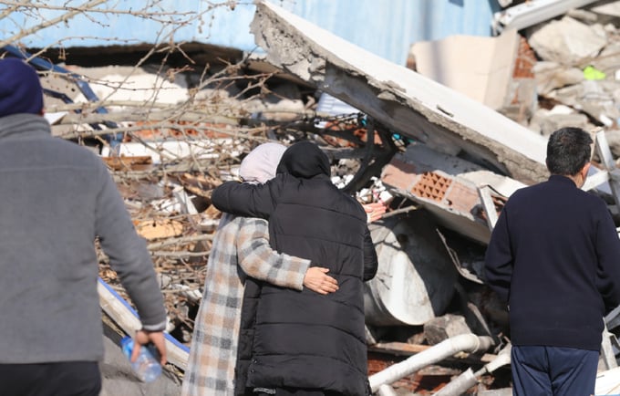 Two women hugging in sorrow in front of a collapsed building