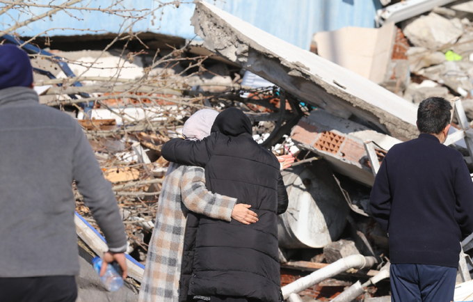 Depremzede iki kadın, çökmüş bir binanın önünde sarılıyor