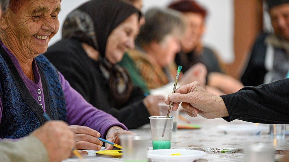 5 yaşlı kişi bir sanat aktivitesi kapsamında bir masanın etrafında oturuyor.