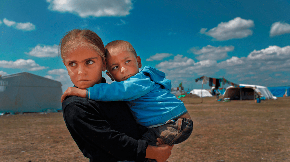 A girl is holding her little sibling in her arms in an open field.