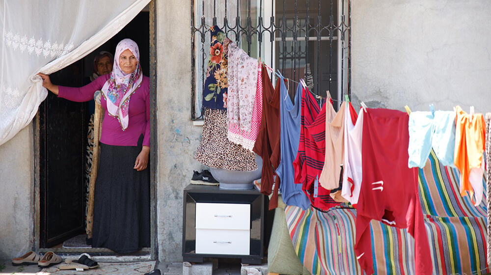 A women is in the yard of her house with clothes are visibly hanging in the garden. 