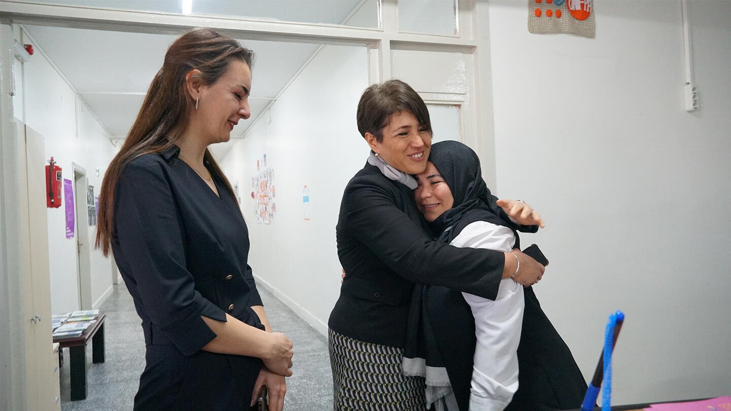 Three women are seen inside UNFPA's center. One of the women holds the other inside her arms.