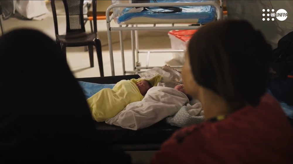 bir çadır hastanesi ortamında kadınların arkasından bebekler görünür.